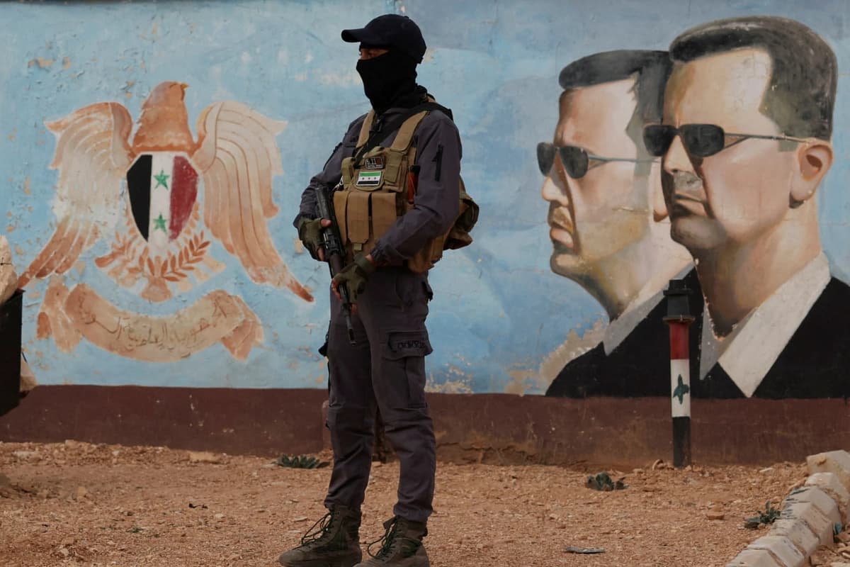 Un miembro del antiguo grupo rebelde Hayat Tahrir al-Sham monta guardia cerca de una imagen de Bashar al-Asad de Siria en el cuartel general de la cuarta división en Damasco, el 23 de enero de 2025. (Yamam Al Shaar/Reuters).