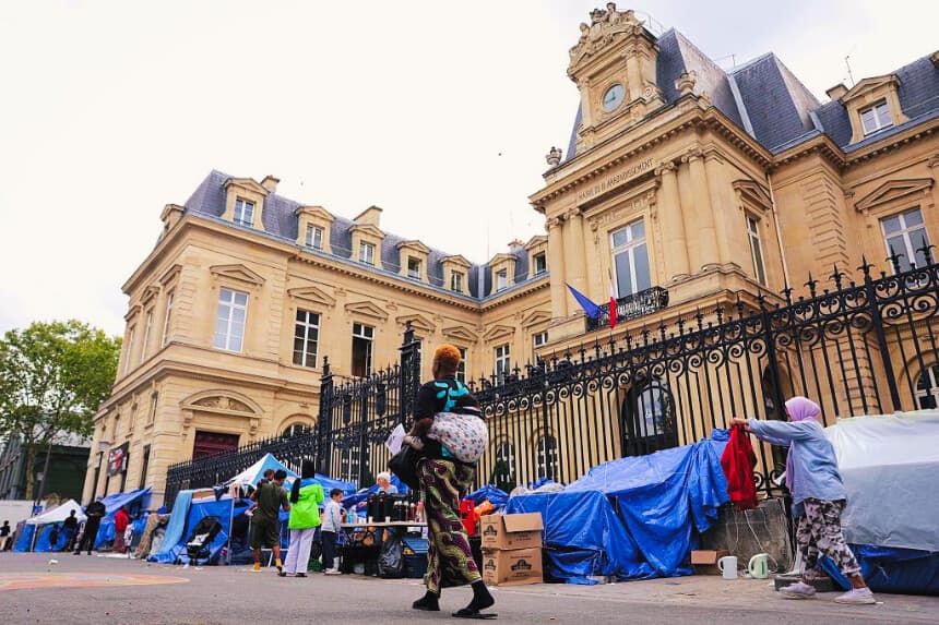 Los migrantes caminan entre las tiendas de campaña de un campamento improvisado en el centro de París, frente al ayuntamiento de París Centro, el 21 de agosto de 2026. (Thomas SAMSON / AFP vía Getty Images)