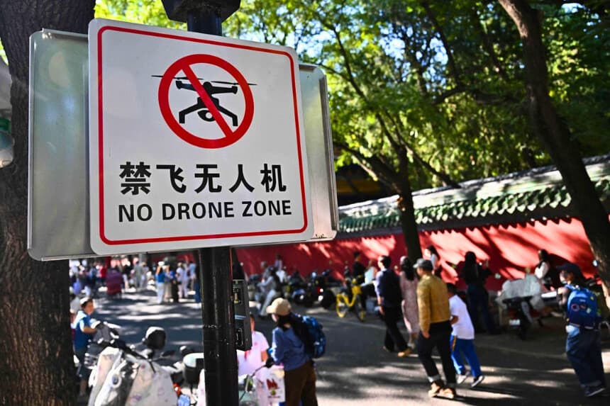 Personas pasan junto a un cartel que dice "Zona prohibida para drones" en un callejón de Pekín el 14 de septiembre de 2026. (Pedro Pardo / AFP vía Getty Images).