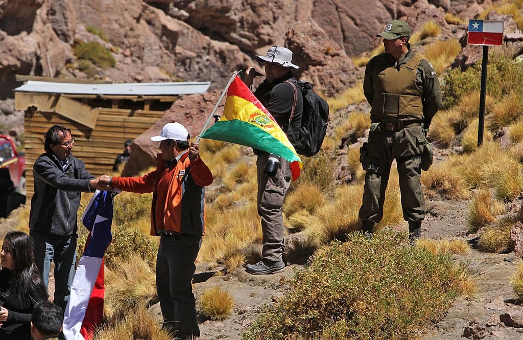 Un chileno (izquierda) y un boliviano, con sus respectivas banderas nacionales en la mano, se dan la mano en la frontera entre Bolivia y Chile, vista desde el departamento de Potosí, Bolivia, el 29 de marzo de 2016. (AIZAR RALDES/AFP vía Getty Images)