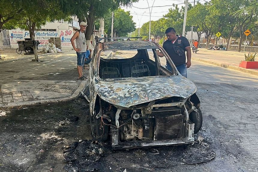 La gente inspecciona un auto quemado tras una operación militar del Ejército colombiano contra el grupo armado relacionado con el narcotráfico "Autodefensa Conquistadoras de la Sierra Nevada" (ACSN) en Santa Marta, Colombia, el 22 de septiembre de 2026. (Idinael FERNÁNDEZ / AFP vía Getty Images)