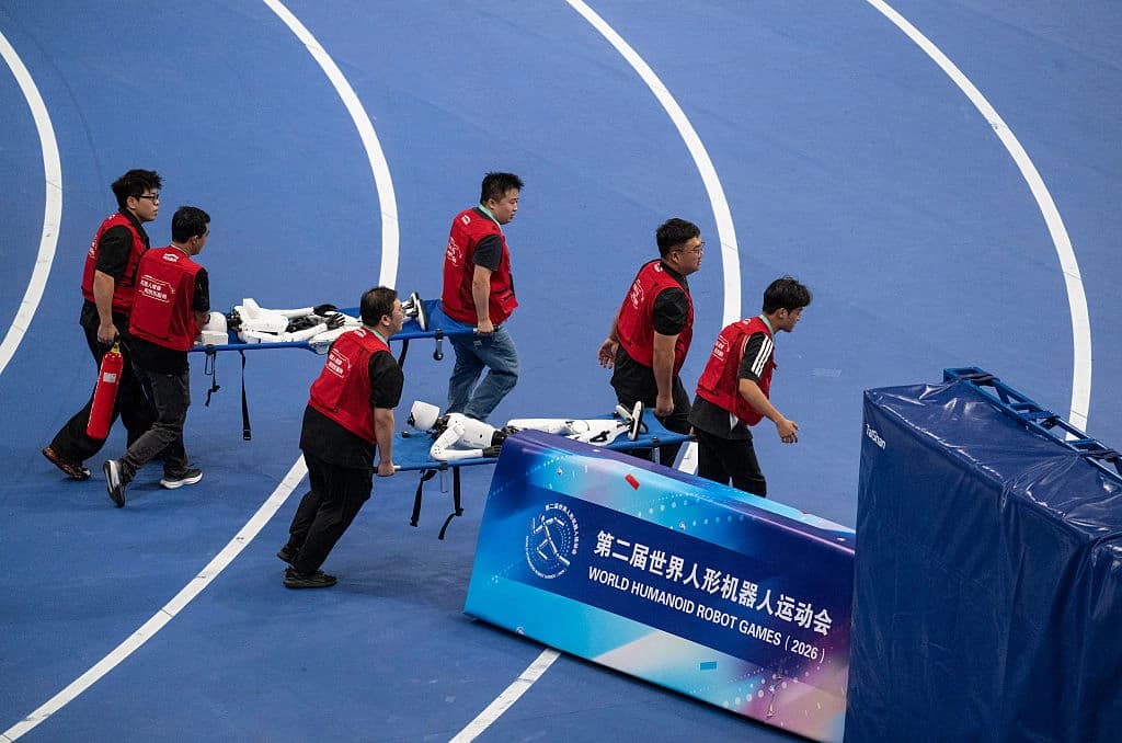 Trabajadores de pista transportan robots humanoides en camillas tras chocar contra la barrera de seguridad en la zona de meta de la final de los 100 metros en la categoría de robots pequeños en los segundos Juegos Mundiales de Robótica celebrados en el Óvalo Nacional de Patinaje de Velocidad el 26 de agosto de 2026. (Kevin Frayer/Getty Images).