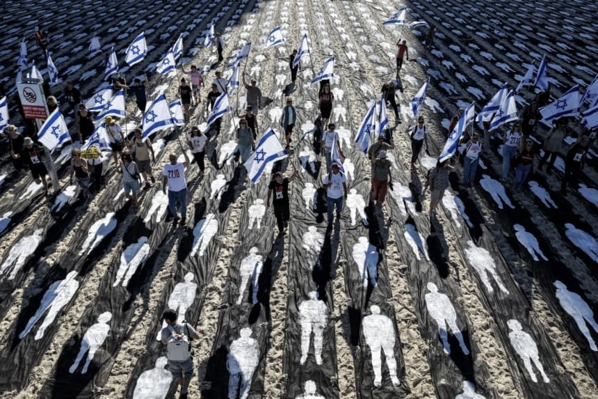 Una vista aérea muestra a personas ondeando banderas israelíes mientras se encuentran en una instalación conmemorativa montada en la playa para conmemorar el tercer aniversario del ataque de Hamás contra Israel del 7 de octubre, en Tel Aviv, el 7 de octubre de 2026. (Jack Guez/AFP vía Getty Images)