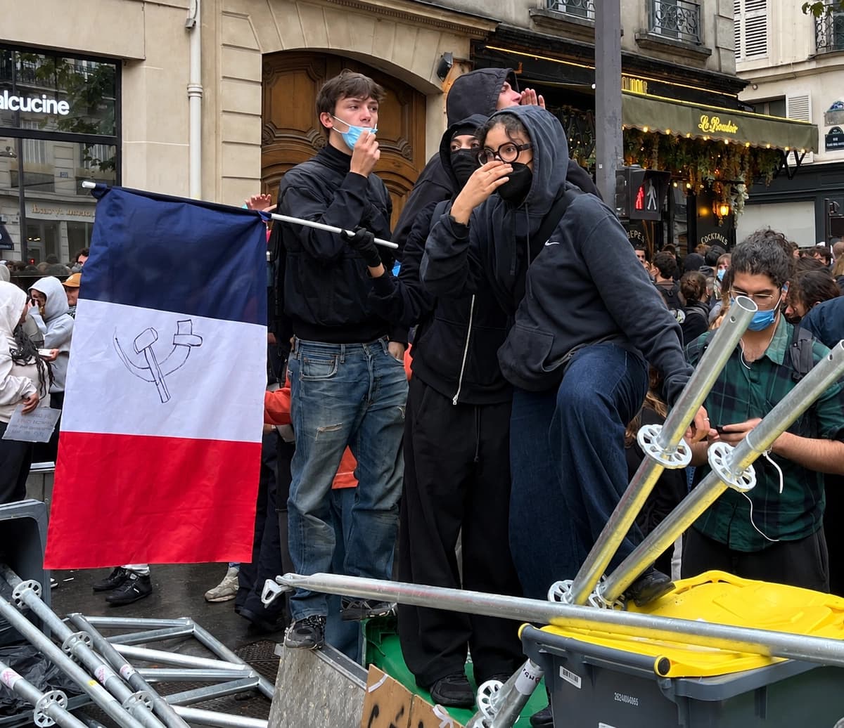 Manifestantes se congregan tras una barricada improvisada cerca de Sciences Po París, junto a una bandera tricolor francesa modificada para incluir el símbolo comunista de la hoz y el martillo, durante el bloqueo estudiantil del 7 de octubre de 2026. (Etienne Fauchaire/The Epoch Times).