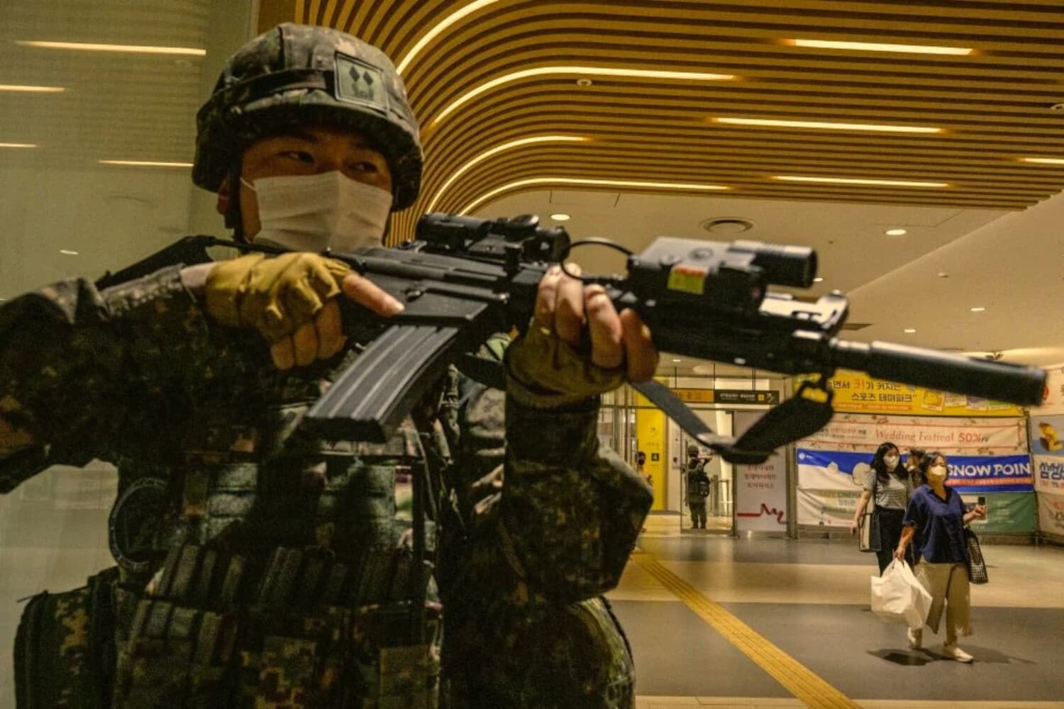 Varios ciudadanos (D) pasan por delante mientras un soldado surcoreano participa en un simulacro, en un centro comercial de Seúl el 23 de agosto de 2022. (ANTHONY WALLACE/AFP vía Getty Images)