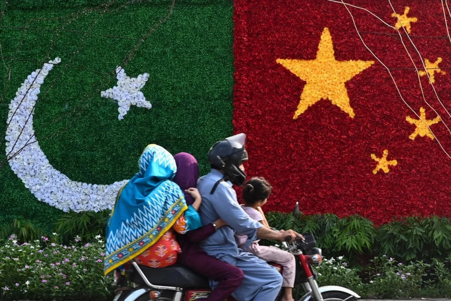 Una familia pasa junto a una decoración con la forma de las banderas de China y Pakistán instalada a lo largo de una carretera con motivo de la visita del viceprimer ministro chino He Lifeng, en Lahore, el 30 de julio de 2023. (Arif Ali/AFP vía Getty Images).