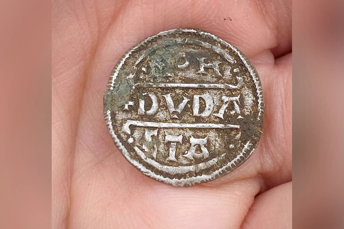 Una de las monedas de plata del tesoro de Bickmarsh reposa en la palma de la mano de quien la encontró tras ser desenterrada. (Servicio de Archivo y Arqueología de Worcestershire)