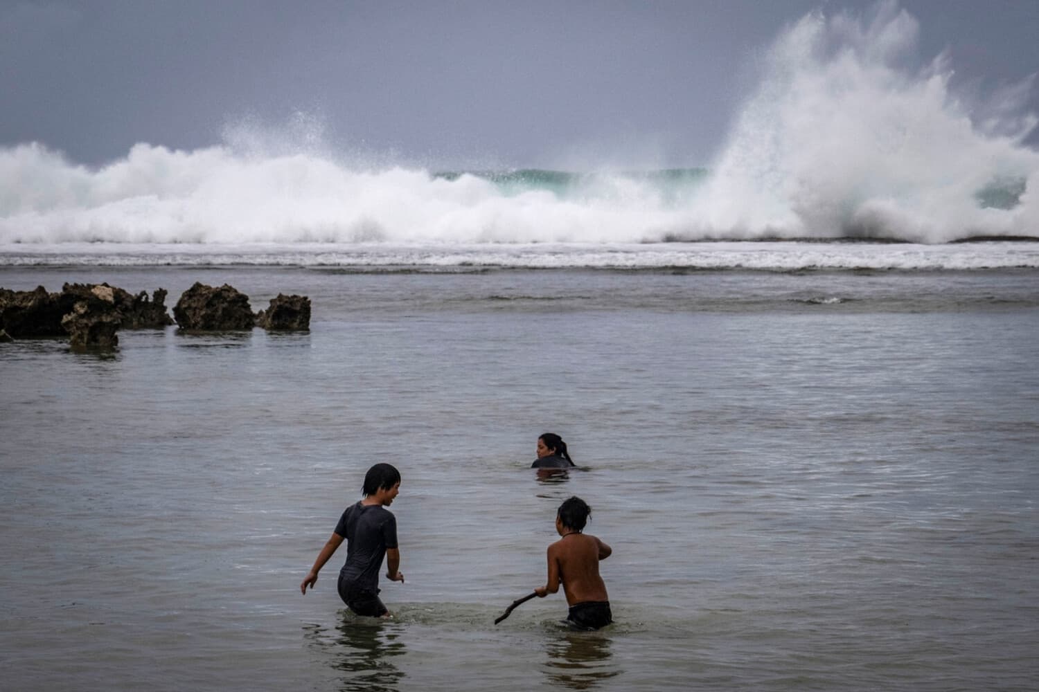 Las olas rompen en la costa mientras los niños juegan en la playa antes de la llegada del supertifón Bavi, según las previsiones, a Guam, en las Islas Marianas del Norte, el 4 de julio de 2026. (Yuichi Yamazaki / AFP vía Getty Images).