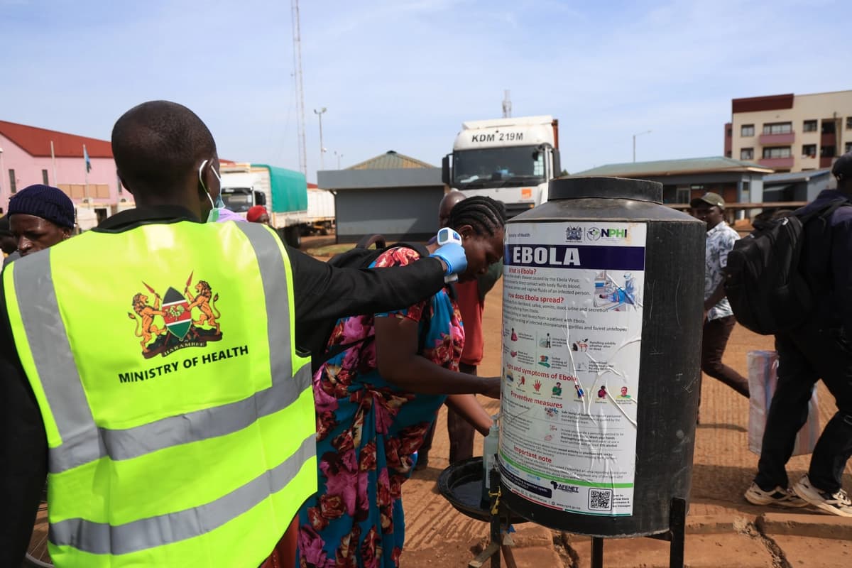 Varias personas se desinfectan las manos mientras un trabajador sanitario toma la temperatura de los viajeros que cruzan de Uganda a Kenia, en Busia, Kenia, el 15 de octubre de 2026. (Foto de Andrew Kasuku/AP).