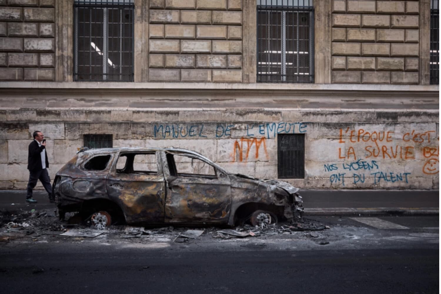Un hombre pasa junto a un automóvil calcinado en la Rue Yves Toudic, destruido tras un fin de semana de protestas en el centro de París el 19 de octubre de 2026. (Kiran Ridley/AFP vía Getty Images).