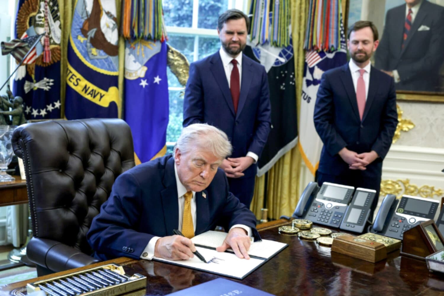 El presidente Donald Trump firma una orden ejecutiva, junto al vicepresidente JD Vance (segundo desde la izquierda) y al presidente de la Comisión Federal de Comercio, Andrew Ferguson (derecha), en el Despacho Oval de la Casa Blanca, en Washington, el 16 de marzo de 2026. (Alex Wong/Getty Images).