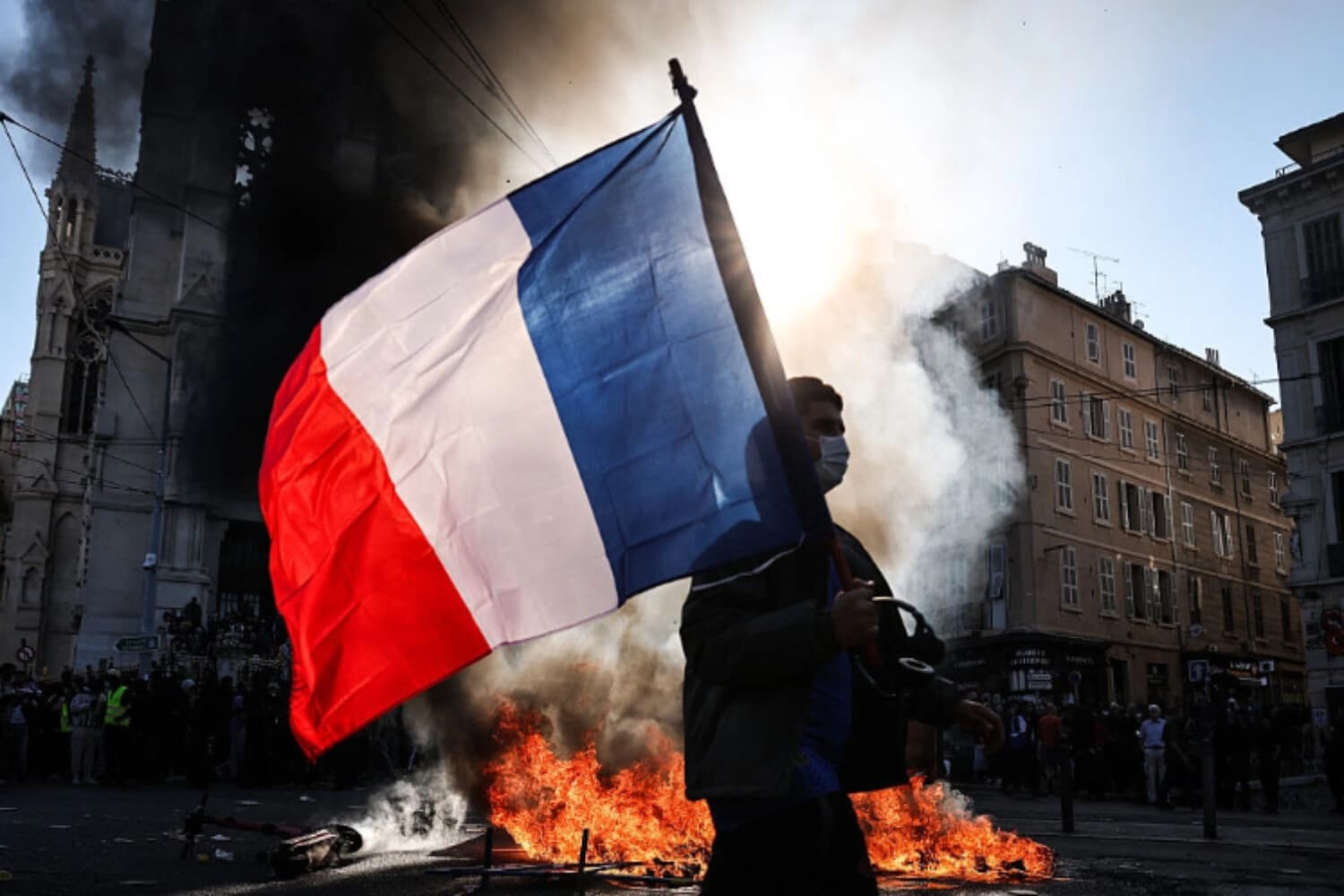 Un hombre que ondea una bandera nacional francesa pasa junto a un incendio en Marsella, Francia, el 17 de octubre de 2026. (Thibaud Moritz/AFP vía Getty Images).