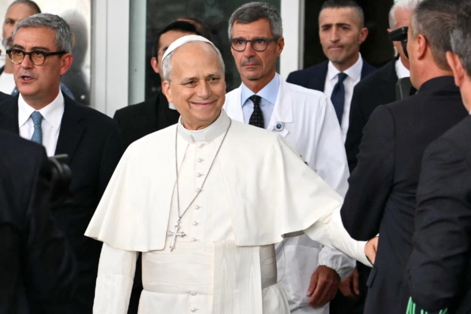 El papa León XIV, acompañado por su cirujano Stefano Margaritora, saluda a la gente al abandonar el Hospital Universitario Gemelli, cuatro días después de una intervención quirúrgica para extirpar un tumor canceroso de su pulmón derecho, en Roma, el 17 de octubre de 2026. (Alberto Pizzoli/AFP vía Getty Images).