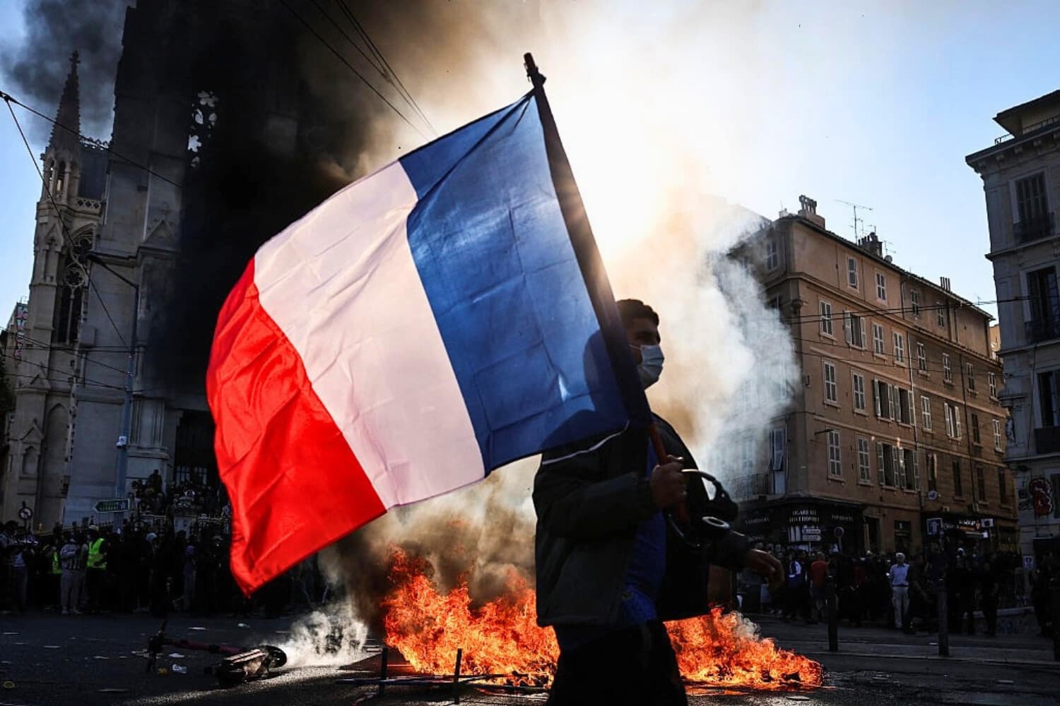 Un hombre que agita una bandera nacional francesa pasa junto a un incendio en Marsella, Francia, el 17 de octubre de 2026. (Thibaud Moritz/AFP vía Getty Images).