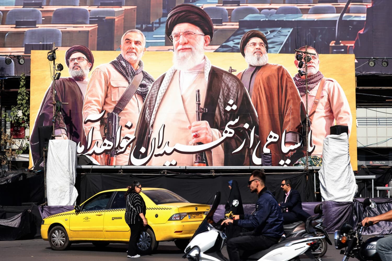 Los viajeros pasan junto a una gran valla publicitaria en la que aparece el líder supremo asesinado, el ayatolá Ali Jamenei (C), en Teherán, el 26 de octubre de 2026. (ATTA KENARE / AFP vía Getty Images)