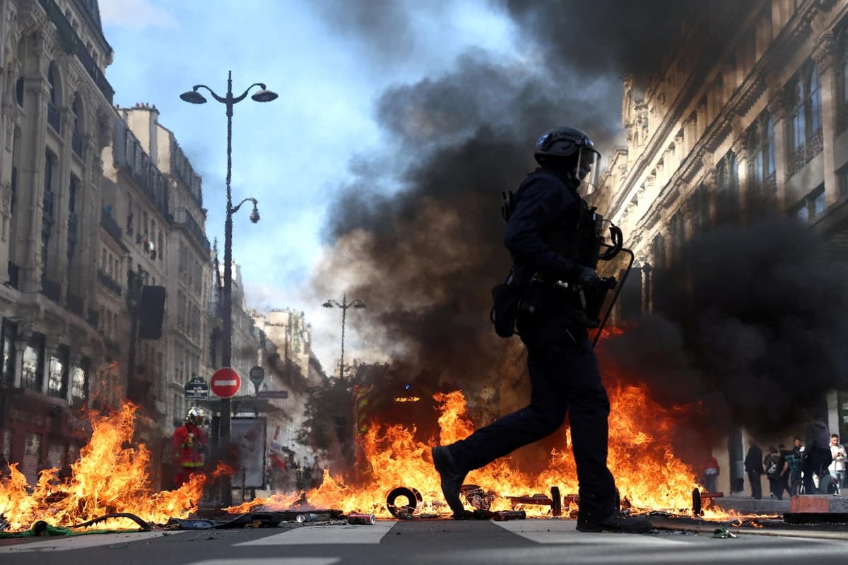 Policías antidisturbios franceses pasan junto a objetos en llamas en una calle durante los enfrentamientos con manifestantes en París el 17 de octubre de 2026. (Abdul Saboor/Reuters).
